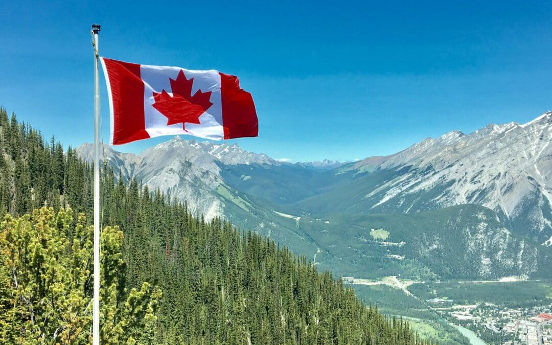 Canadian flag waving in front of a mountain range on a clear day.
